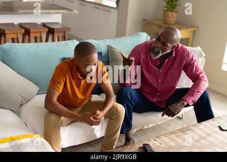 African american male teenager talking with his father and sitting on couch Stock Photo