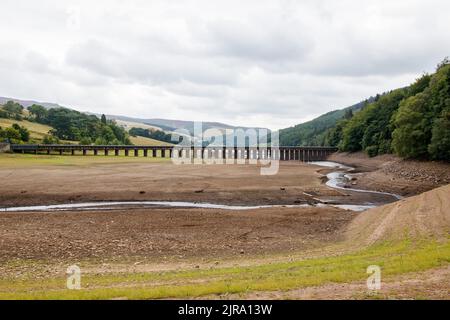 The water level is reduced to a small stream at the Upper end of the Ladybower reservoir near the visitor centre. The Ladybower reservoir during the dry and drought weather in the summer of 2022. Ladybower Reservoir is a large Y-shaped, artificial reservoir, the lowest of three in the Upper Derwent Valley in Derbyshire, England. Stock Photo