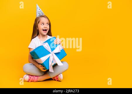 Full length photo of funky impressed school girl wear white t-shirt birthday cap present empty space isolated yellow color background Stock Photo