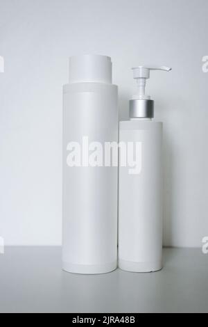 Two cosmetic plastic bottles with pump dispenser isolated on grey background. Beauty products packaging mock up. Body cream or lotion containers. Stock Photo