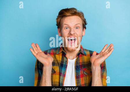 Photo of astonished handsome crazy guy with ginger hair wear plaid shirt open mouth palms up shouting isolated on blue color background Stock Photo