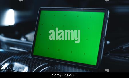 Modern tablet computer with chromakey green screen on the opened bonnet of a car during maintenance and repairing in a car service Stock Photo
