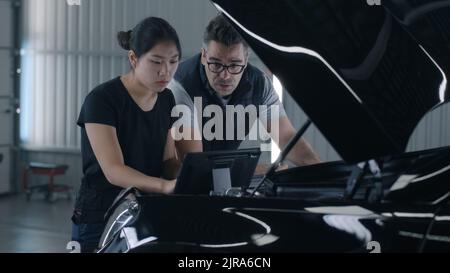 Male and female employees near the hood diagnosing and checking a car together in a car service using a tablet and discussing repairing Stock Photo