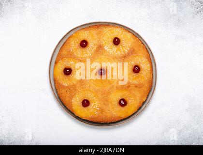 Homemade pineapple upside down cake with glace cherries on a light rustic background. Delicious vegetarian sweet food concept. Stock Photo