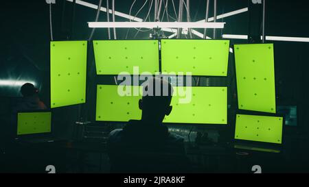 Zoom in view unrecognizable man writing malicious code on computers while sitting against computer monitors with chromakey screens in dark room of hacker base Stock Photo