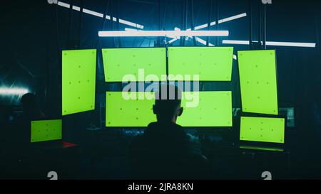 Zoom in view unrecognizable man writing malicious code on computers while sitting against computer monitors with chromakey screens in dark room of hacker base Stock Photo