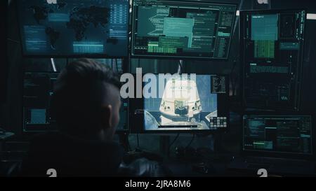 Male programmer using computer to control space unit and station coupling process while sitting at table in dark room. Footage furnished by NASA. Stock Photo