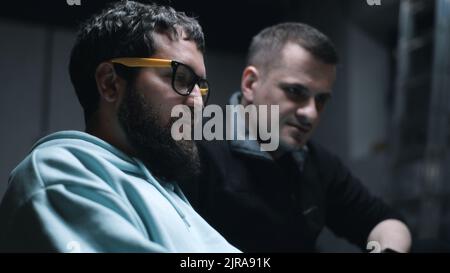 Programmer with laptop and IT director of a company talking and discussing work together in a bomb shelter during the war Stock Photo