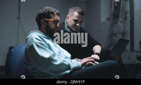 Programmer with laptop and IT director of a company talking and discussing work together in a bomb shelter during the war Stock Photo