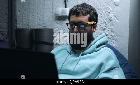 Male IT worker in glasses working on a website in a laptop and programming during war in the basement Stock Photo