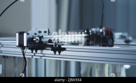 Soft focus of printing mechanism moving on 3D printer during plastic model creation in contemporary workshop Stock Photo