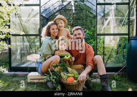 Farmer family with fresh harvest sitting in a greenhouse Stock Photo