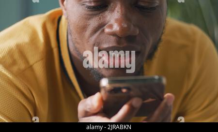 African American male in yellow t shirt talking and sending audio message on smartphone Stock Photo
