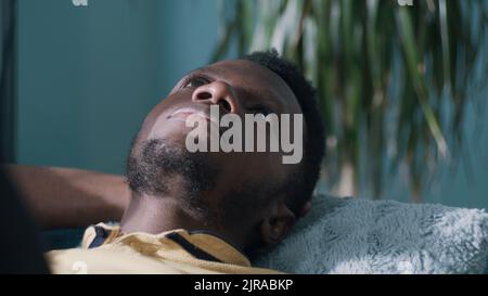 Pensive black guy looking up and thinking while lying on sofa alone at home Stock Photo