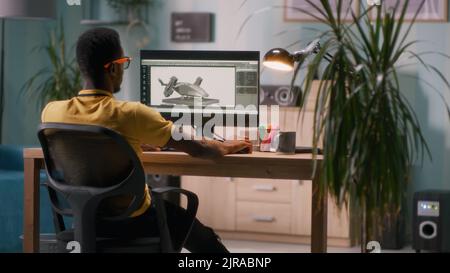 African American man creating 3D model and video for videogame on computer while sitting at table in light workplace at home Stock Photo