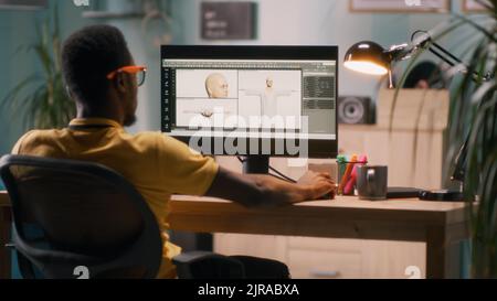African American man using computer to create 3D model of human for videogame during work from home Stock Photo