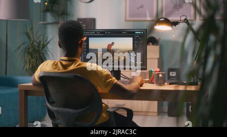 Back view of African American man using software on computer to create visual effects on video with chromakey background during work in home office Stock Photo