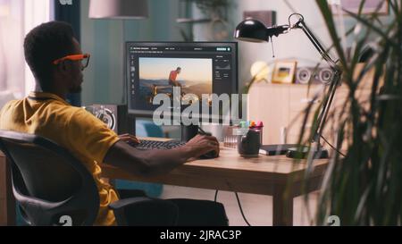 Back view of African American man using software on computer to create visual effects on video with chromakey background during work in home office Stock Photo