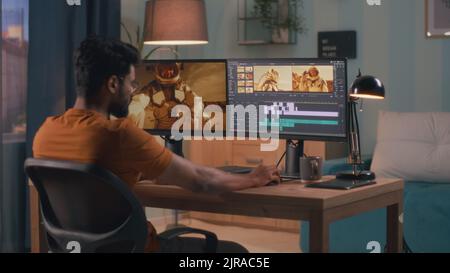 Back view of male content creator using computer to edit cosmonaut video during remote work from home Stock Photo