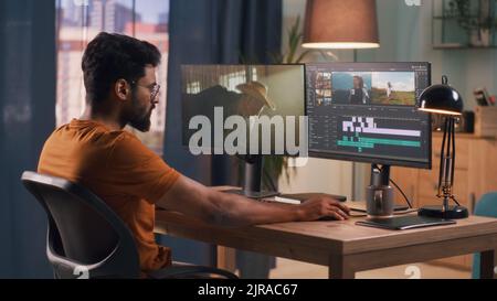 Unrecognizable man in orange t shirt using computer to edit video while sitting at table and working at home Stock Photo