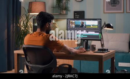 Unrecognizable man in orange t shirt using computer to edit video while sitting at table and working at home Stock Photo