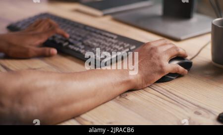 Unrecognizable man sitting at table in workplace and using computer mouse and keyboard Stock Photo