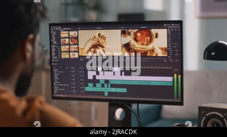 Back view of male content creator using computer to edit cosmonaut video during remote work from home Stock Photo