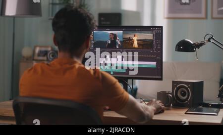 Unrecognizable man in orange t shirt using computer to edit video while sitting at table and working at home Stock Photo