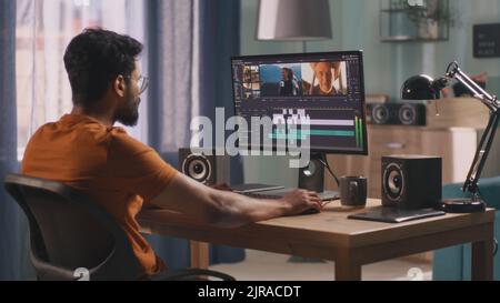 Unrecognizable man in orange t shirt using computer to edit video while sitting at table and working at home Stock Photo