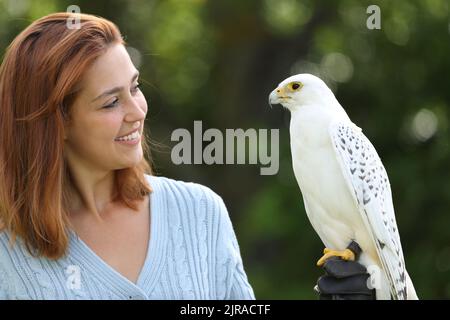Happy woman holding and looking at falcon in nature Stock Photo