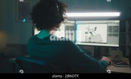 Man in glasses and headphones rendering 3D animation with futuristic aircraft for movie while working remotely from home in evening Stock Photo
