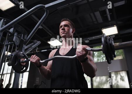 Low angle shot of a bodybuilder looking focused, doing biceps curls with ez curl bar Stock Photo