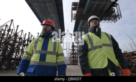 Men in uniform walking under bridge and talking during work on construction site Stock Photo