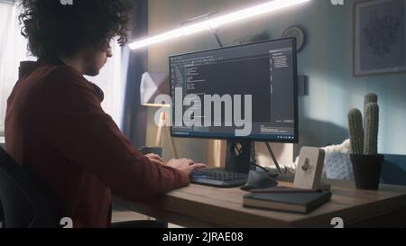 Man with curly hair typing on computer keyboard and creating code while sitting at desk and working remotely from home. Stock Photo