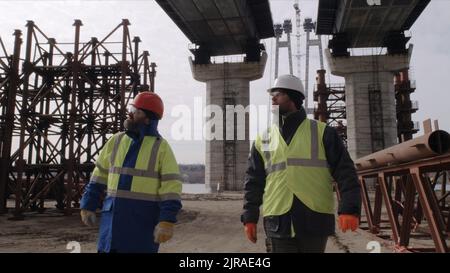 Men in uniform walking under bridge and talking during work on construction site Stock Photo