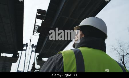 Adult man in hardhat examining concrete structure of unfinished bridge during work on construction site Stock Photo