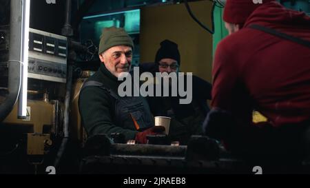 Zoom in view of senior man with drink discussing work on fishing ship with colleagues during break Stock Photo