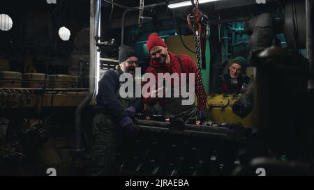 Cheerful adult man showing mobile phone to colleague while working in engine room of fishing ship Stock Photo