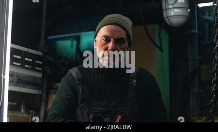 Serious mature man inspecting metal part and talking while working in engine room of ship Stock Photo