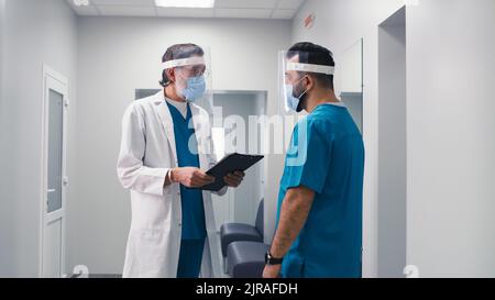 Asian woman in medical uniform and face shield running and calling colleagues during emergency in modern clinic Stock Photo