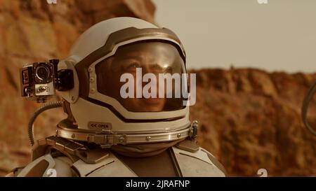 Woman with camera on spacesuit helmet looking around and talking while shooting video during colonization of Mars Stock Photo