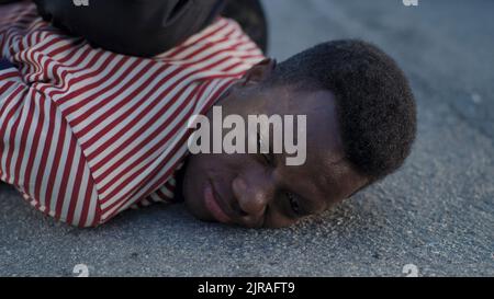 Crop police officer pressing resisting black man to ground and putting on handcuffs then lifting convict during law enforcement operation Stock Photo