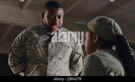 African American commander scolding female soldier under concrete ceiling of military base Stock Photo