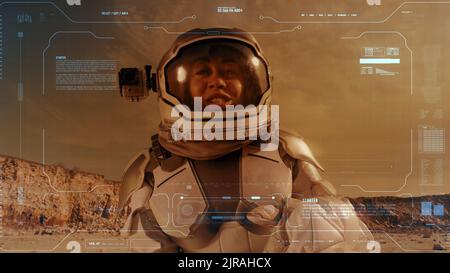 Woman in space suit waving hand and gesturing thumb up while talking about life on Mars for video diary recording with blue interface Stock Photo