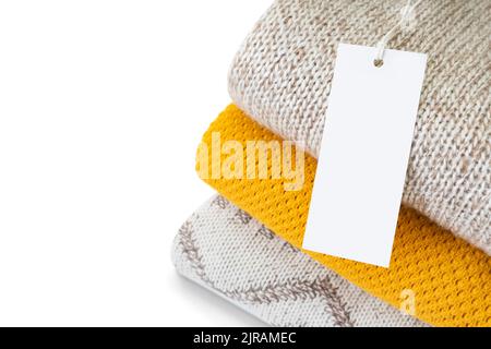 White blank rectangular clothing tag, label mockup template on heap of knitted clothes isolated on white background . Price tag label with copy space Stock Photo