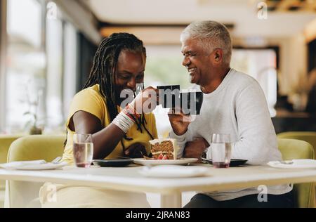 Senior couple laughing cheerfully while eating together in a coffee shop. Happy senior couple having a good time in a restaurant. Mature couple enjoyi Stock Photo