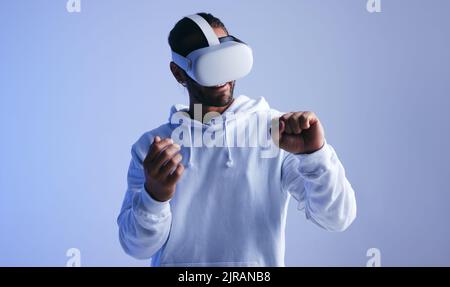 Cheerful young man smiling happily while having an immersive virtual reality experience. Young man looking at his fist through a virtual reality heads Stock Photo