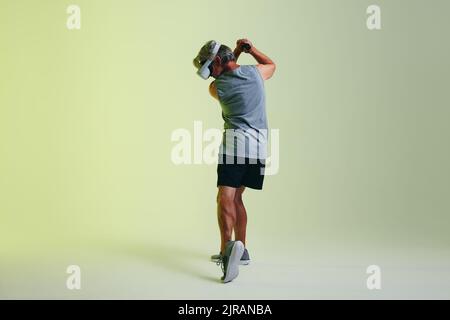 Senior sportsman man playing golf in virtual reality. Mature man swinging a virtual golf club using a pair of gaming controllers. Athletic senior man Stock Photo