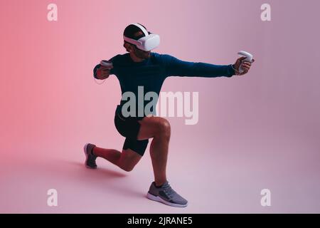 sporty young man playing archery in virtual reality. Young man shooting a virtual arrow using gaming controllers. Active young man wearing a virtual r Stock Photo