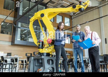 Engineers in factory having meeting in front of industrial robot Stock Photo